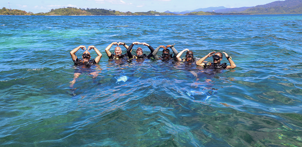 Happy group of scuba divers in Port Barton smiling and showing the OK sign above the water, ready for an exciting dive adventure.